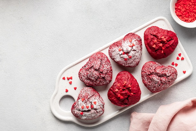 Фото Вкусные красные бархатные кексы в форме сердца, украшенные посыпкой на керамической доске