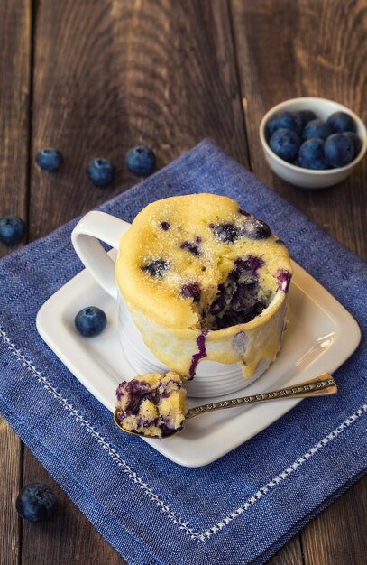 Delicious homemade blueberry muffin mug cake with fresh berries on rustic wooden background