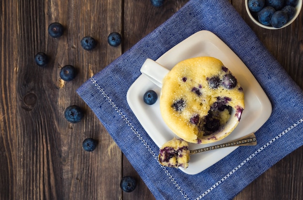 Delicious homemade blueberry muffin mug cake with fresh berries on rustic wooden background