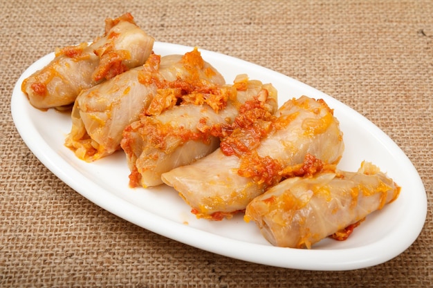 Delicious homemade cabbage rolls stuffed with rice and meat lay on white dish with sackcloth on the background.