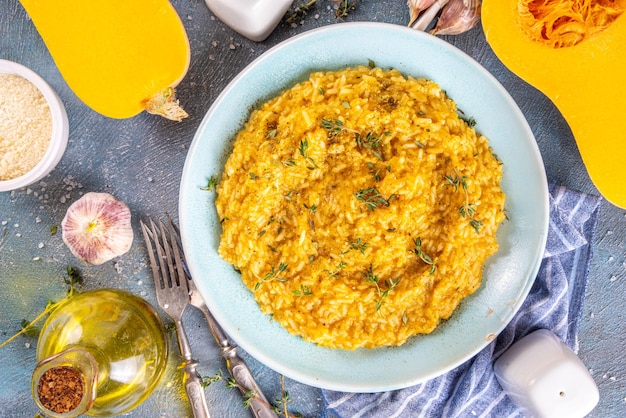 Foto delizioso risotto alla zucca sfoglia di formaggio fatto in casa con parmigiano e timo con ingredienti e spezie su tavolo di cemento blu