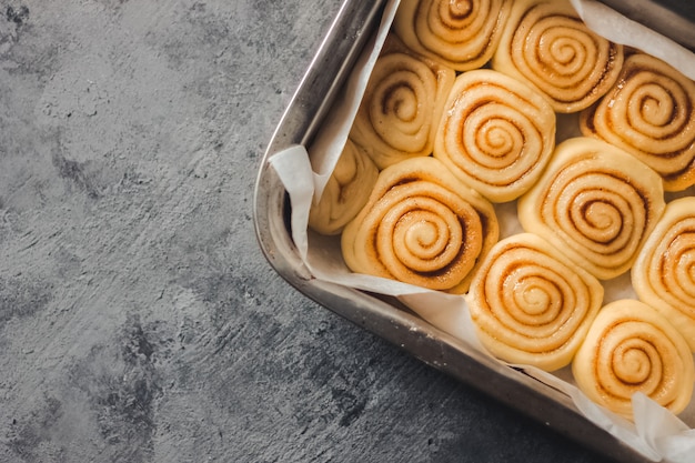 Delicious homemade cinnamon rolls bun dough in rectangle shaped baking tray on the dark grey concrete background.