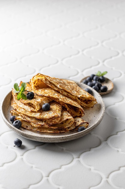 Delicious homemade crepes on ceramic plate with blueberry and mint on white tile background for maslenitsa