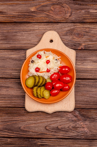 Delicious homemade fermented vegetables on a plate sauerkraut, pickled tomatoes, pickles, wooden surface