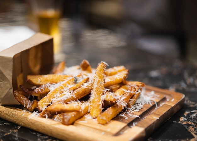 Patata fritta casalinga deliziosa con formaggio tagliuzzato sul piatto di legno