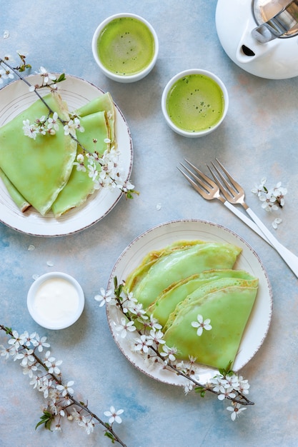 Delicious homemade green pancakes with blossoming cherry tree branches with green matcha tea