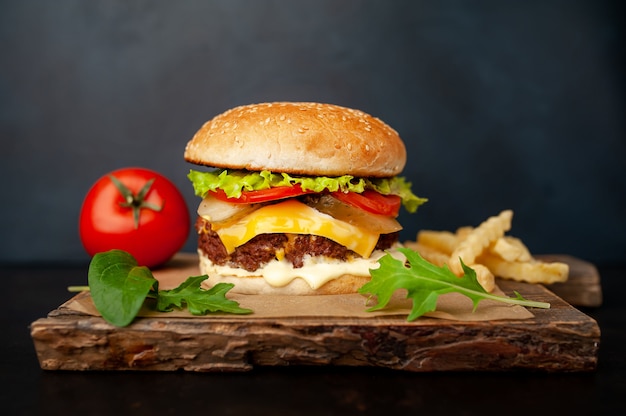 Delicious homemade hamburger with beef, lettuce, cheese, cucumber and french fries on stone background