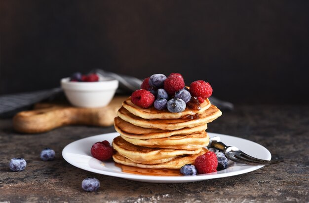 Delicious homemade pancakes in a plate with berries: raspberries, blueberries and maple syrup  .