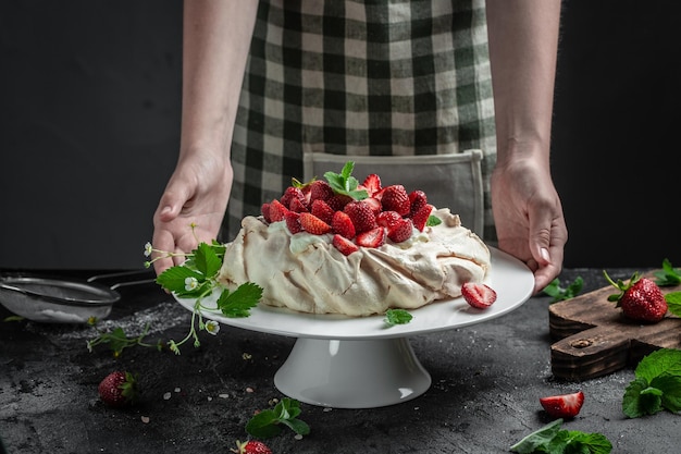 신선한 딸기와 휘핑크림을 곁들인 맛있는 홈메이드 파블로바 케이크 맛있는 머랭 케이크를 장식하는 여성 제빵사 긴 배너 형식