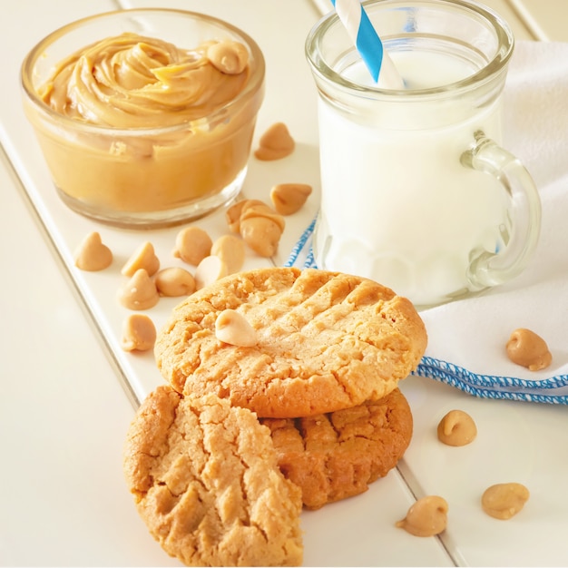 ミルクのマグカップとおいしい自家製ピーナッツバタークッキー。白い木の空間。健康的なスナックやおいしい朝食のコンセプト。正方形の画像。トーンの写真。