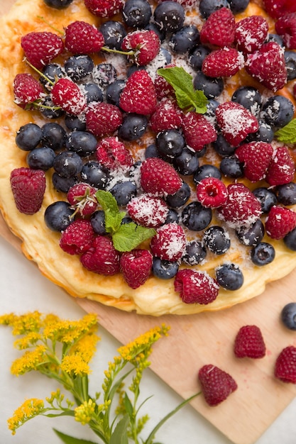 Delicious homemade pie with organic raspberries and blueberries and summer flowers on wooden board