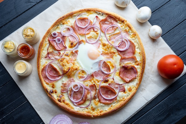 Delicious homemade pizza with ingridients on dark background top view. Flat lay pizza with salami, egg, onion and melted cheese. Viw from above traditional italian cuisine. Food for lunch