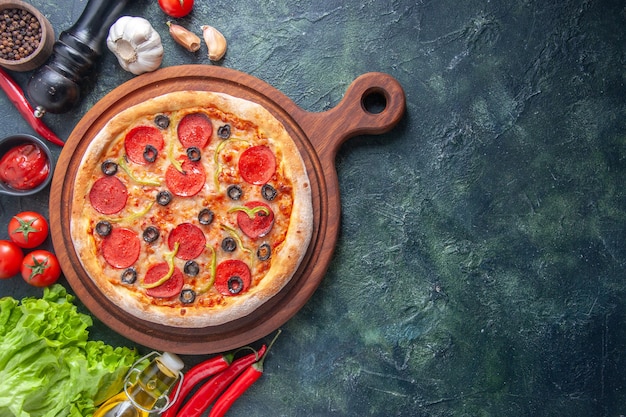 Delicious homemade pizza on wooden cutting board tomatoes ketchup green bundle garlic on the right side on dark surface