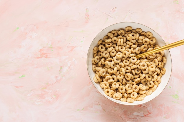 Delicious honey cheerios cereal in a bowl and golden spoon on pink background Top view copy space