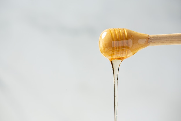 Delicious honey with wooden honey dipper on white wooden surface