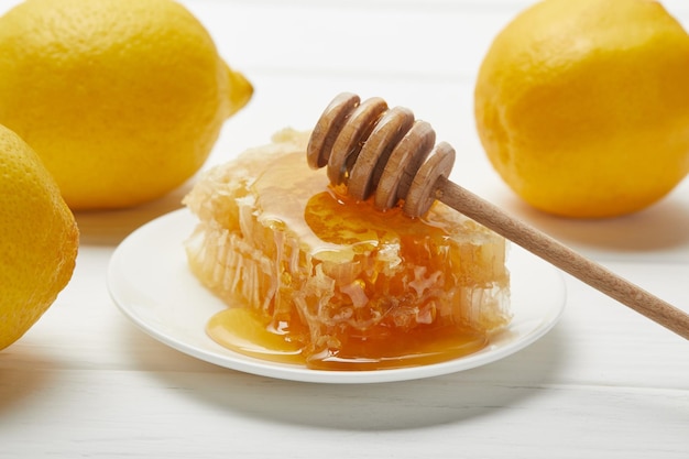 Delicious honeycomb lemons and honey dripper on white wooden table