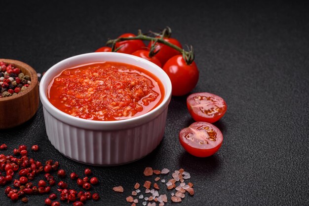 Foto deliziosa salsa rossa piccante piccante con sale e spezie in una ciotola di ceramica su uno sfondo di cemento scuro