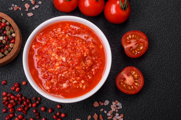 Delicious hot spicy red sauce with salt and spices in a ceramic bowl on a dark concrete background