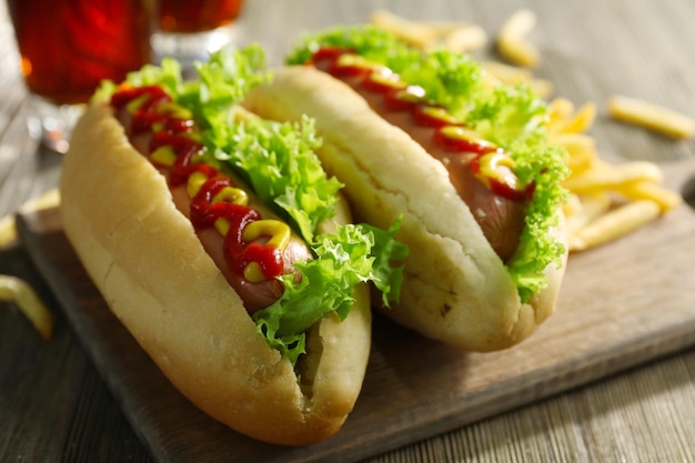 Delicious hotdogs with French fries on wooden chopping board close up