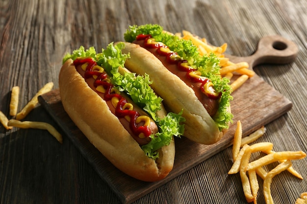 Delicious hotdogs with French fries on wooden chopping board