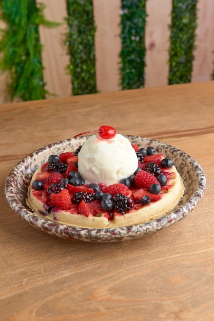 Delicious ice cream waffle with red fruits and cherry on wooden table