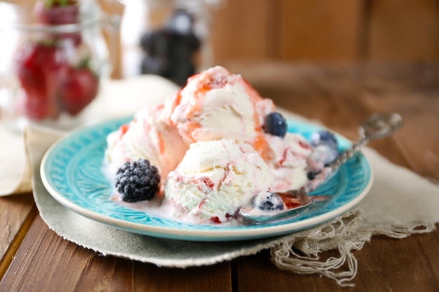 Delicious ice cream with fresh frozen berries and sauce on wooden background