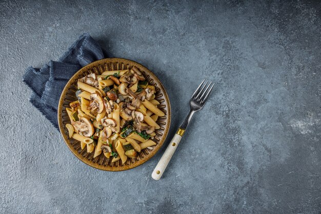 Photo delicious italian dish, penne pasta with spanach, zucchini and roasted mushrooms with garlic on the blue marble textured table. integral pasta and whole champignon mushrooms