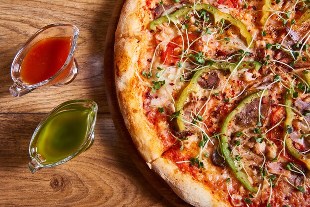 おいしいイタリアのピザは、木製のテーブルにトマトとガーリックソースを添えてください。トップビュー、クローズアップ