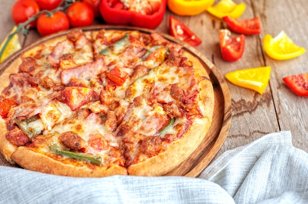 Delicious Italian pizza sliced with bacon, cheese, tomato, capsicum on wooden plate