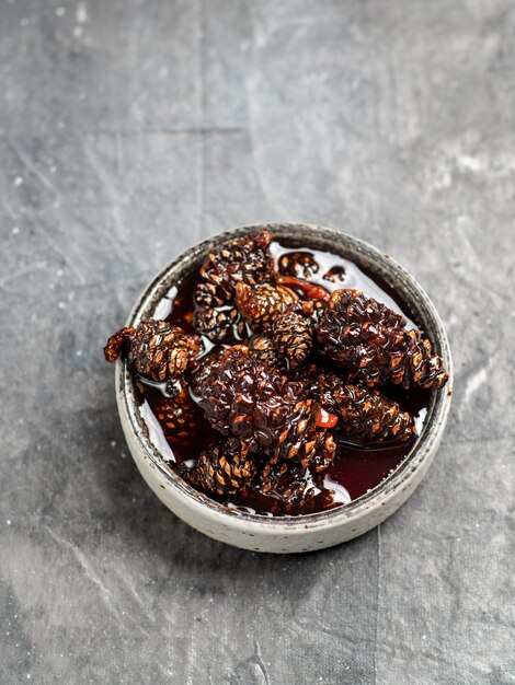 Delicious jam with baby pine cones in small bowl. Traditional Siberian dessert with young pine cones jam on gray texture