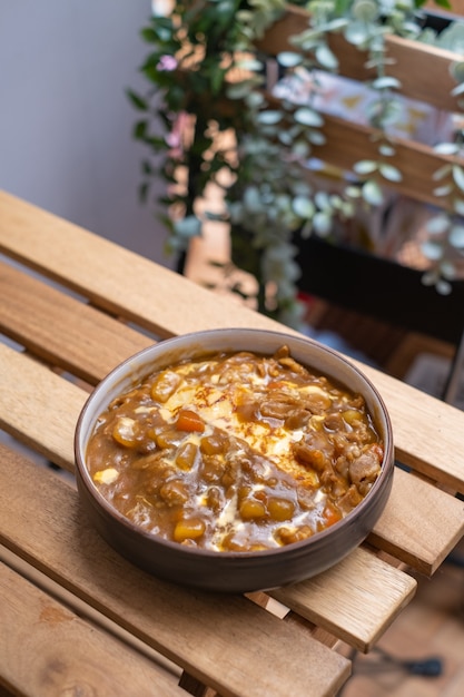 맛있는 일본 고기 카레는 오믈렛 쌀과 야채와 함께 제공되며, 복사 공간이 있는 나무 테이블에 검은 접시에 카레 라이스가 제공됩니다.