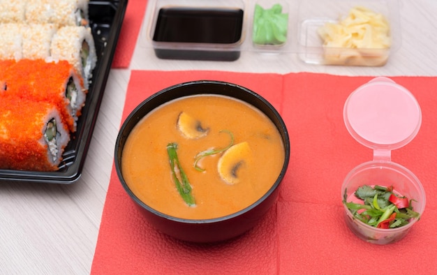 Delicious Japanese tom yum soup rolls with salmon avocado cucumber cheese in takeout packaging with wood sticks and soy sauce Selective focus Asian food and delivery concept Healthy eating