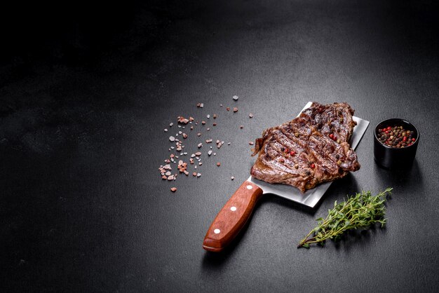 Delicious juicy fresh beef steak with spices and herbs on a dark concrete background. Grilled dishes