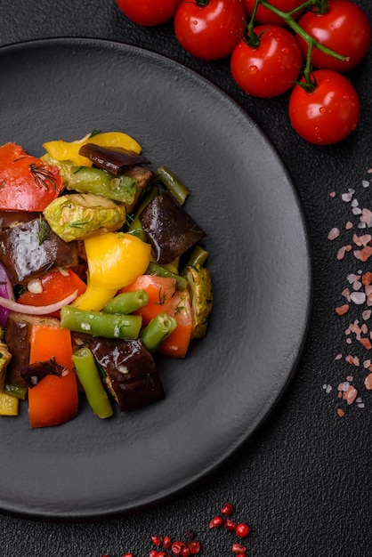 Delicious juicy fresh salad of baked eggplant tomatoes zucchini onions spices and salt on a dark concrete background