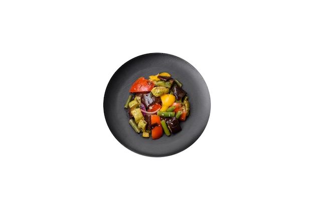 Фото Вкусный сочный свежий салат из запеченных баклажанов, помидоров, цуккини, лука, специй и соли на темном бетонном фоне.