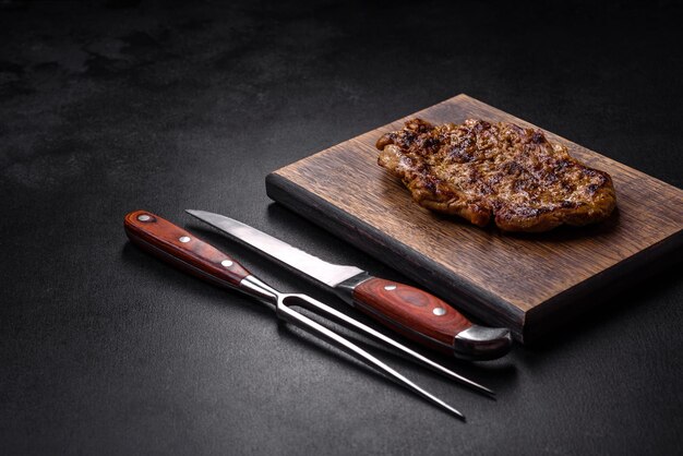 Delicious juicy grilled pork steak with spices and herbs on a wooden cutting board