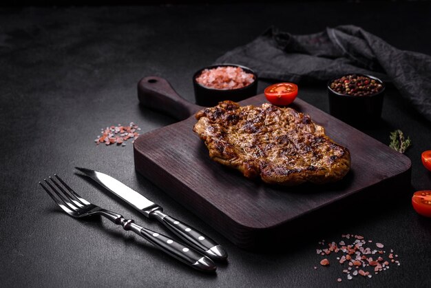 Delicious juicy grilled pork steak with spices and herbs on a wooden cutting board