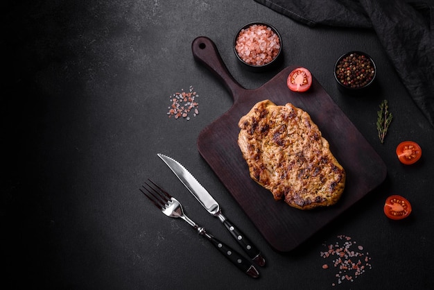 Delicious juicy grilled pork steak with spices and herbs on a wooden cutting board