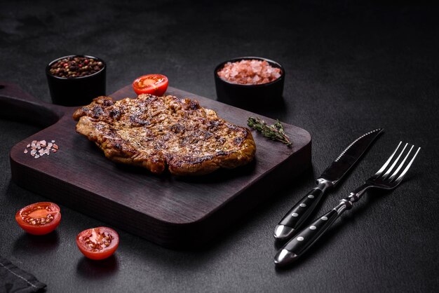 Delicious juicy grilled pork steak with spices and herbs on a wooden cutting board