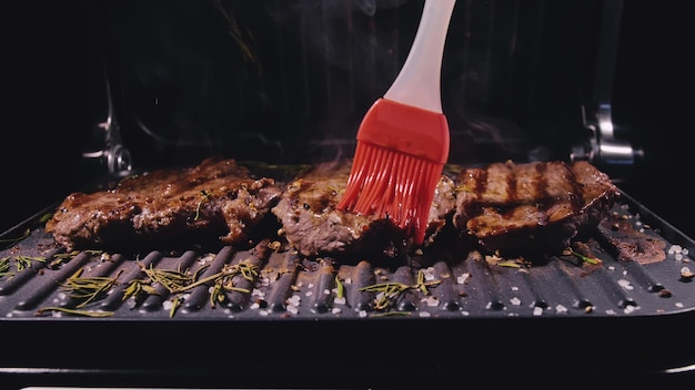 Delicious juicy meat steak cooking on grill prime rare roast\
grilling beef electric roaster rosemary black pepper salt silicone\
cooking brush