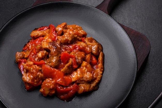 Delicious juicy meat with hot peppers and sauce on a black ceramic plate on a dark concrete background