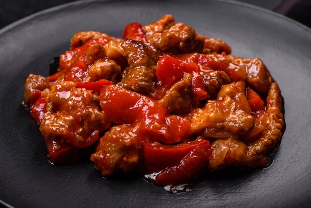 Photo delicious juicy meat with hot peppers and sauce on a black ceramic plate on a dark concrete background