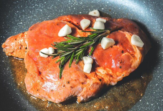 Delicious juicy pork steak seasoned with rosemary and garlic is fried in a pan.