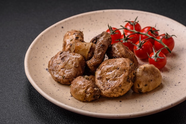 Delicious juicy whole champignons baked on the grill with salt and spices on a ceramic plate on a dark concrete background