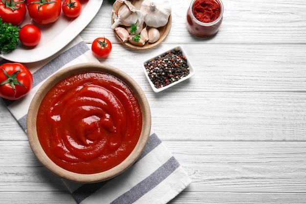 Delicious ketchup in bowl with ingredients on wooden background top view