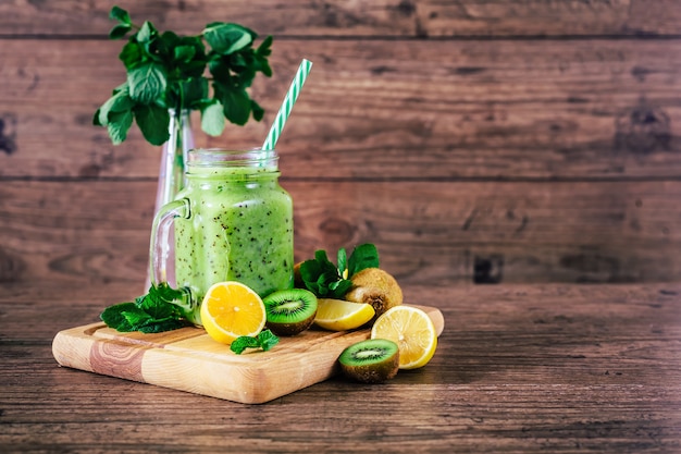 Delicious kiwi smoothie with mint in mason jar on table against dark wooden background