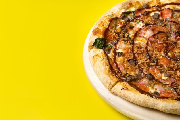 Delicious large pizza with bacon and spinach on a yellow background