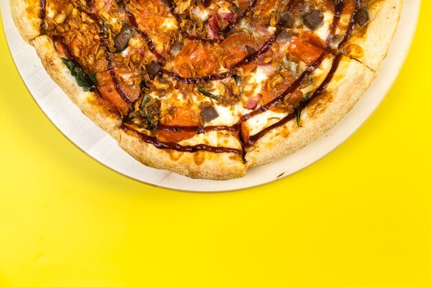Delicious large pizza with bacon and spinach on a yellow background
