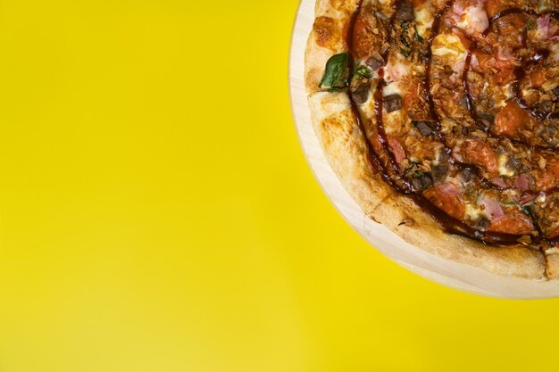 Delicious large pizza with bacon and spinach on a yellow background