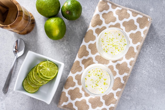 Delicious lemon mousse on a brown tablecloth and white table background with whole and sliced lemons in the background and a metal spoon